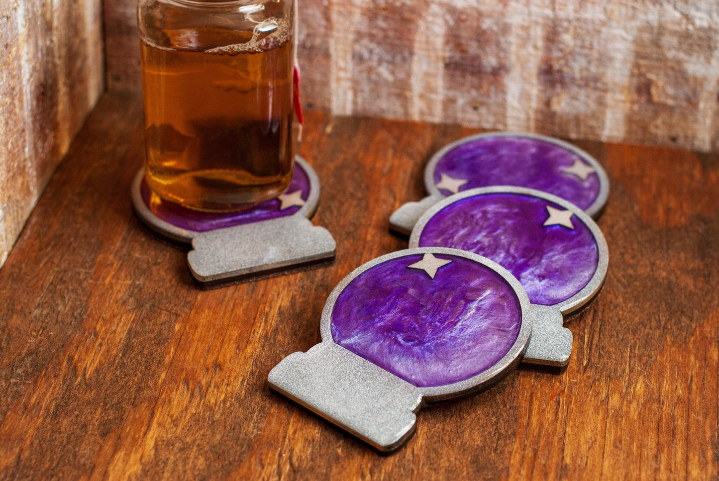 A set of purple and silver mystical celestial-themed resin crystal ball coasters with a star on a wooden surface and glass of tea