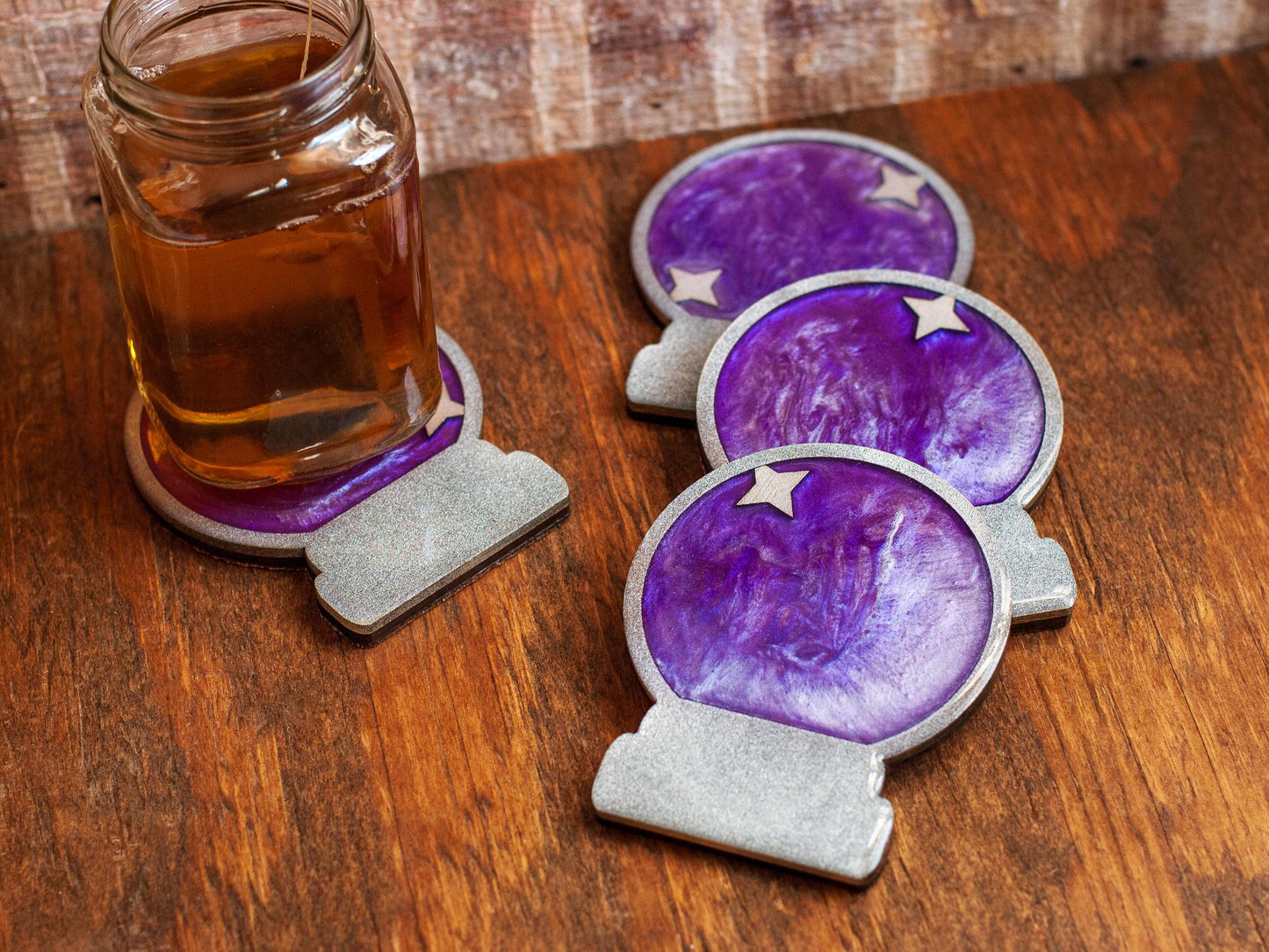 Purple and silver mystical crystal ball coasters on a wooden surface with a glass of tea