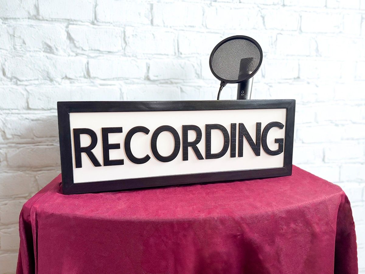 black recording studio light sign and podcast microphone on a table with red tablecloth