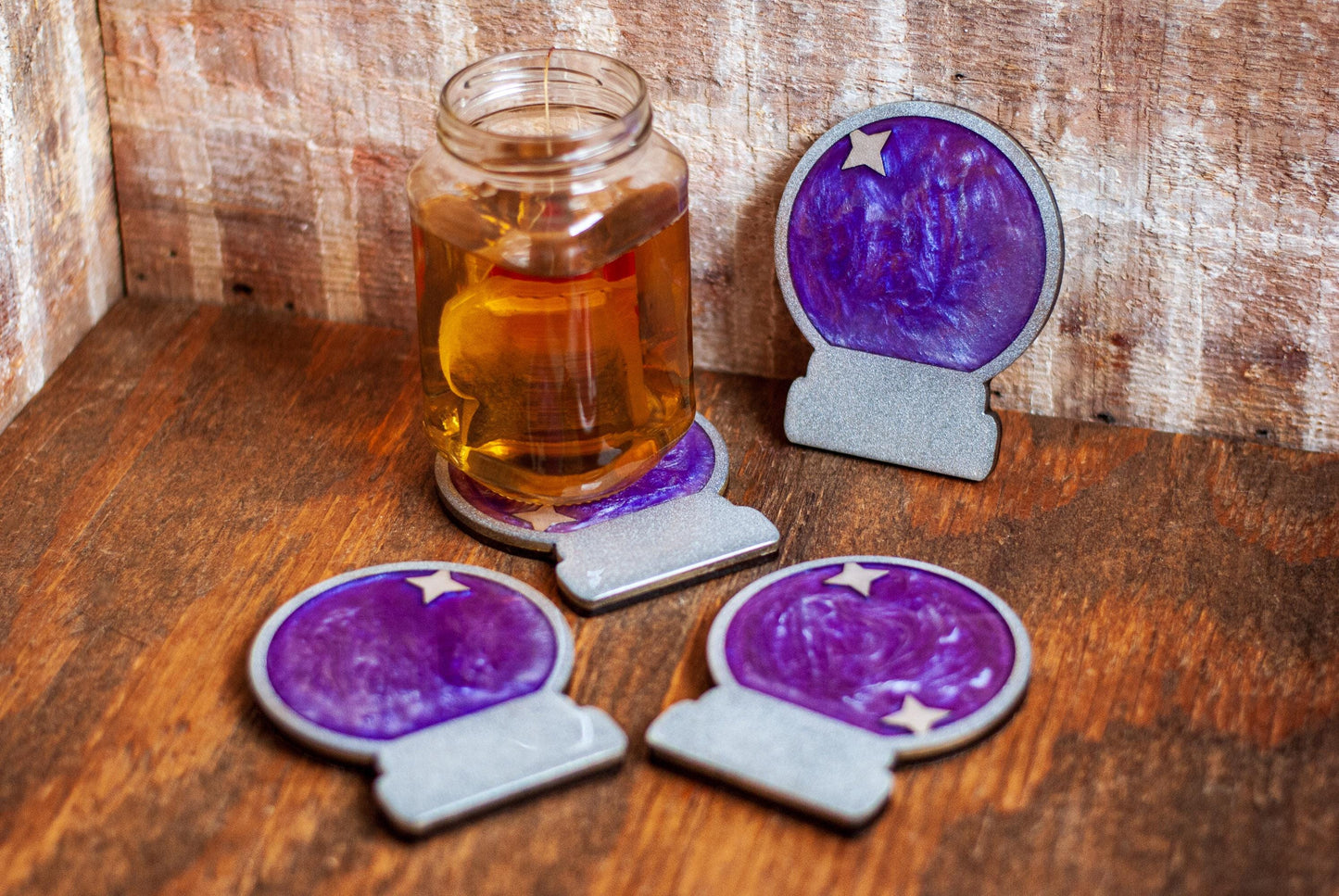 A set of two purple and silver mystical celestial-themed resin crystal ball coasters on a wooden table and cup of tea