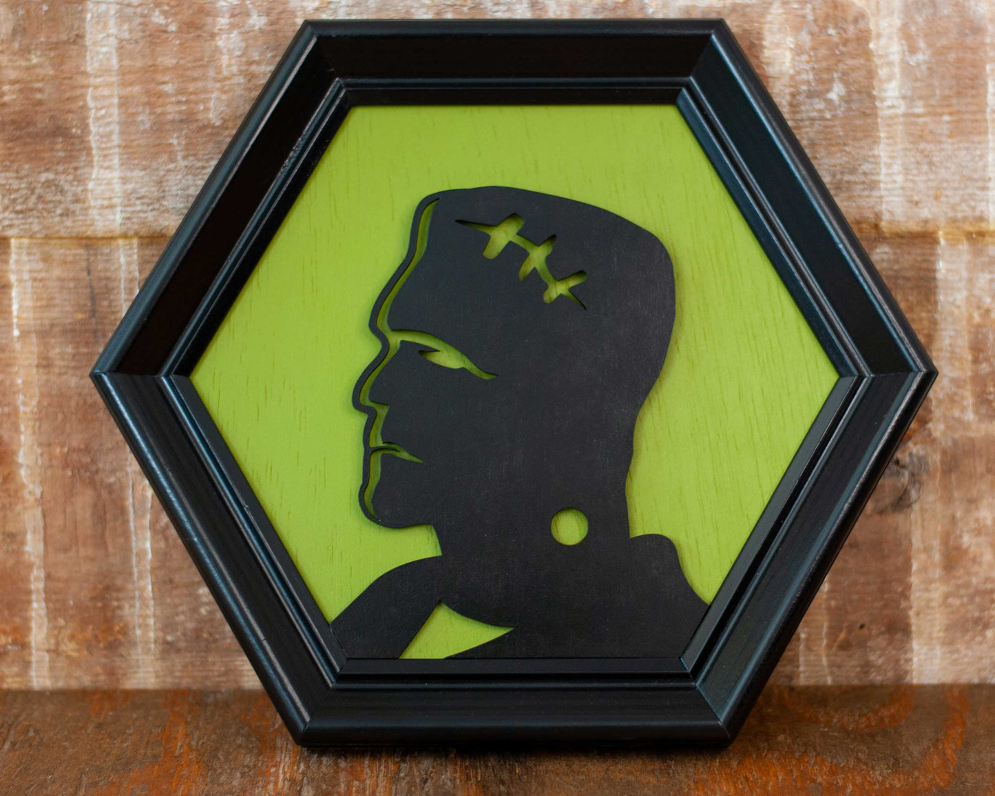 Hexagonal frame with a black silhouette of a modern Frankenstein on a green background against a brick wall.
