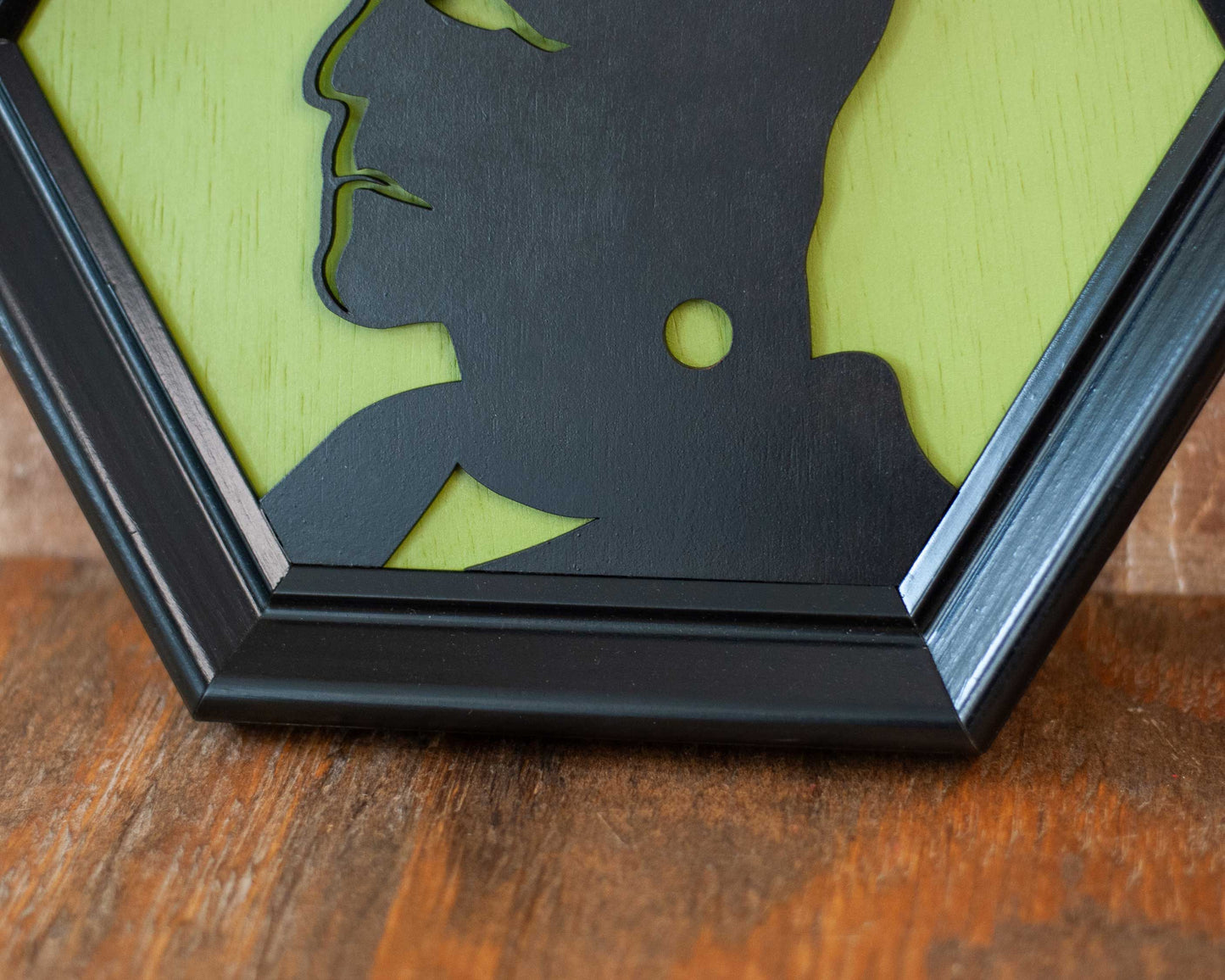 Hexagonal frame with a black silhouette of a modern Frankenstein on a green background against a brick wall.