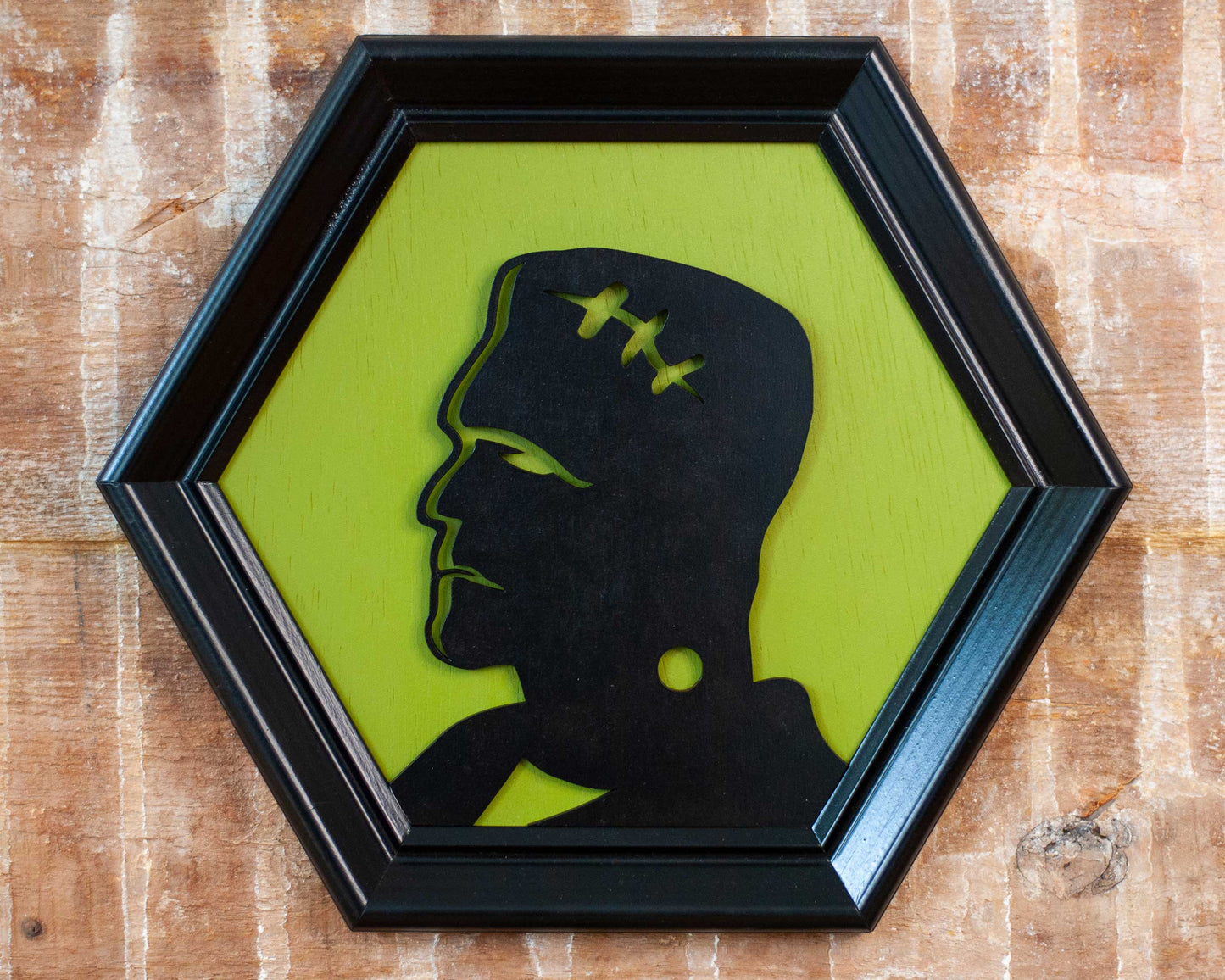 Hexagonal frame with a black silhouette of a modern Frankenstein on a green background against a brick wall.