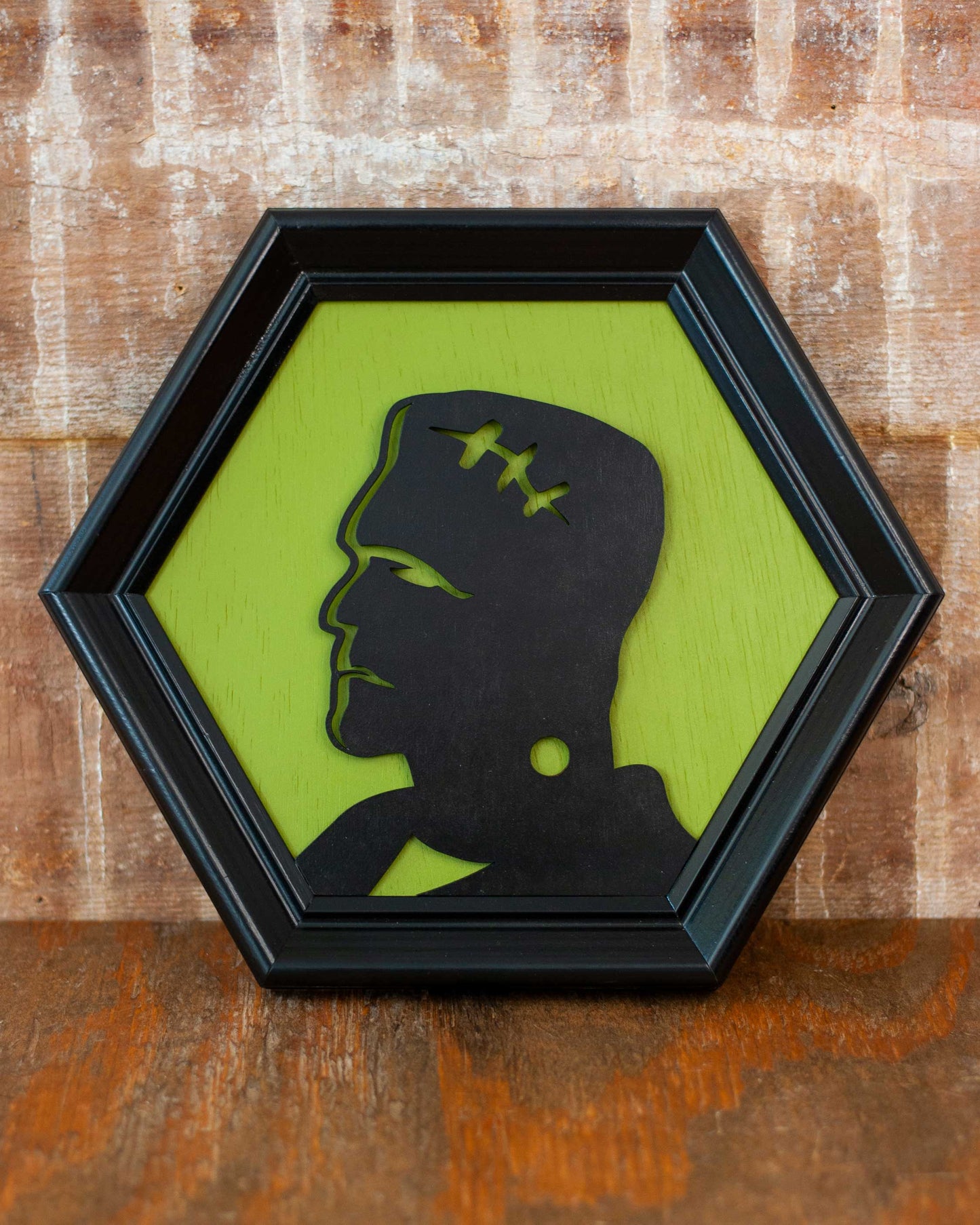 Hexagonal frame with a black silhouette of a modern Frankenstein on a green background against a brick wall.