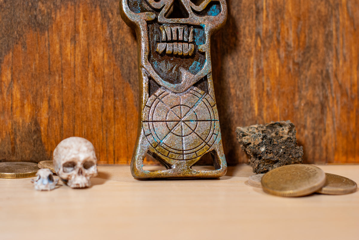 Close up view of a copper bones skeleton key prop on a wooden surface with coins and small rocks.