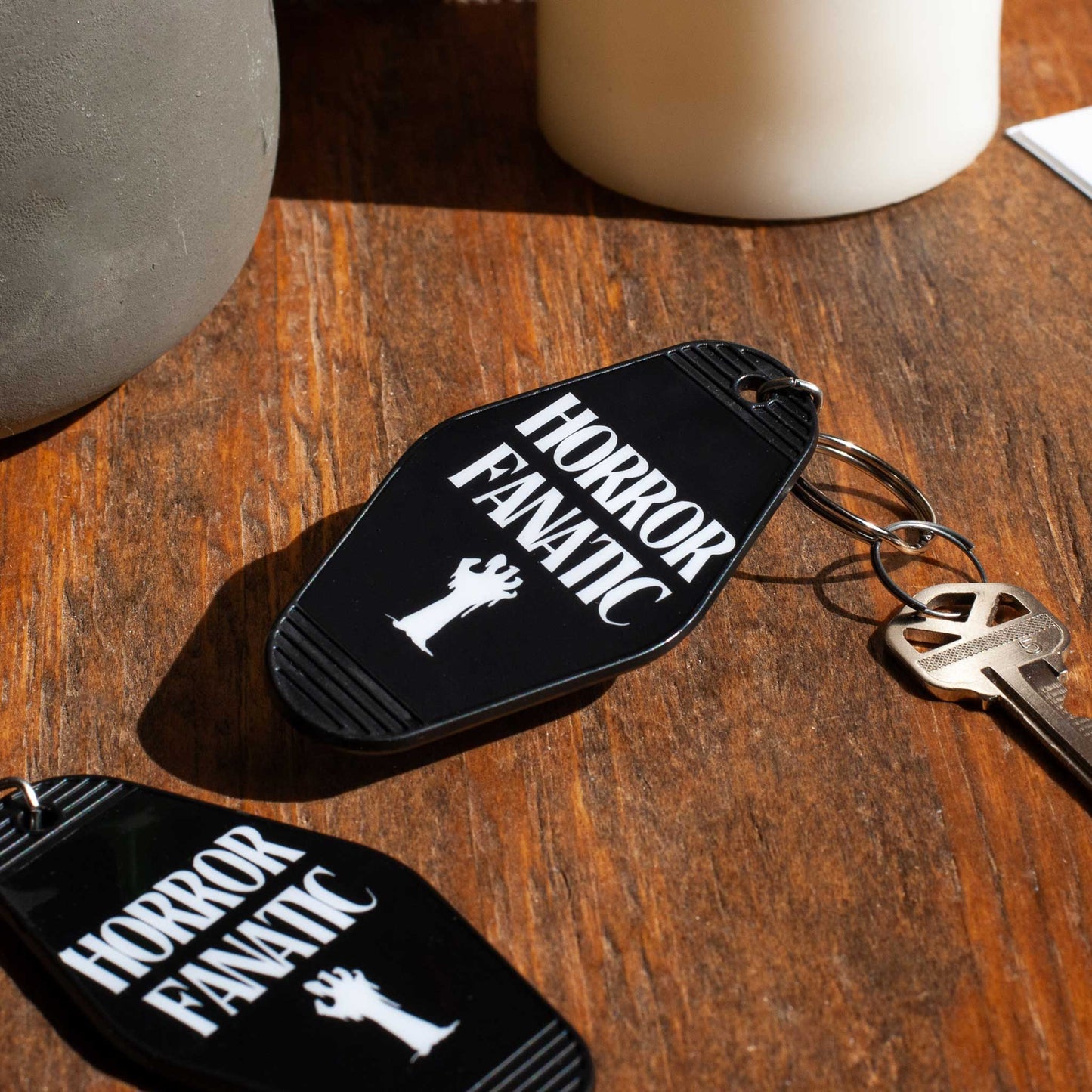 Black motel keychain with 'Horror Fanatic' text on a wooden surface