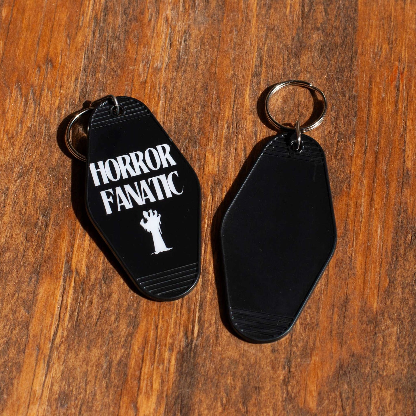 back view of a black motel keychain with 'Horror Fanatic' text on a wooden surface