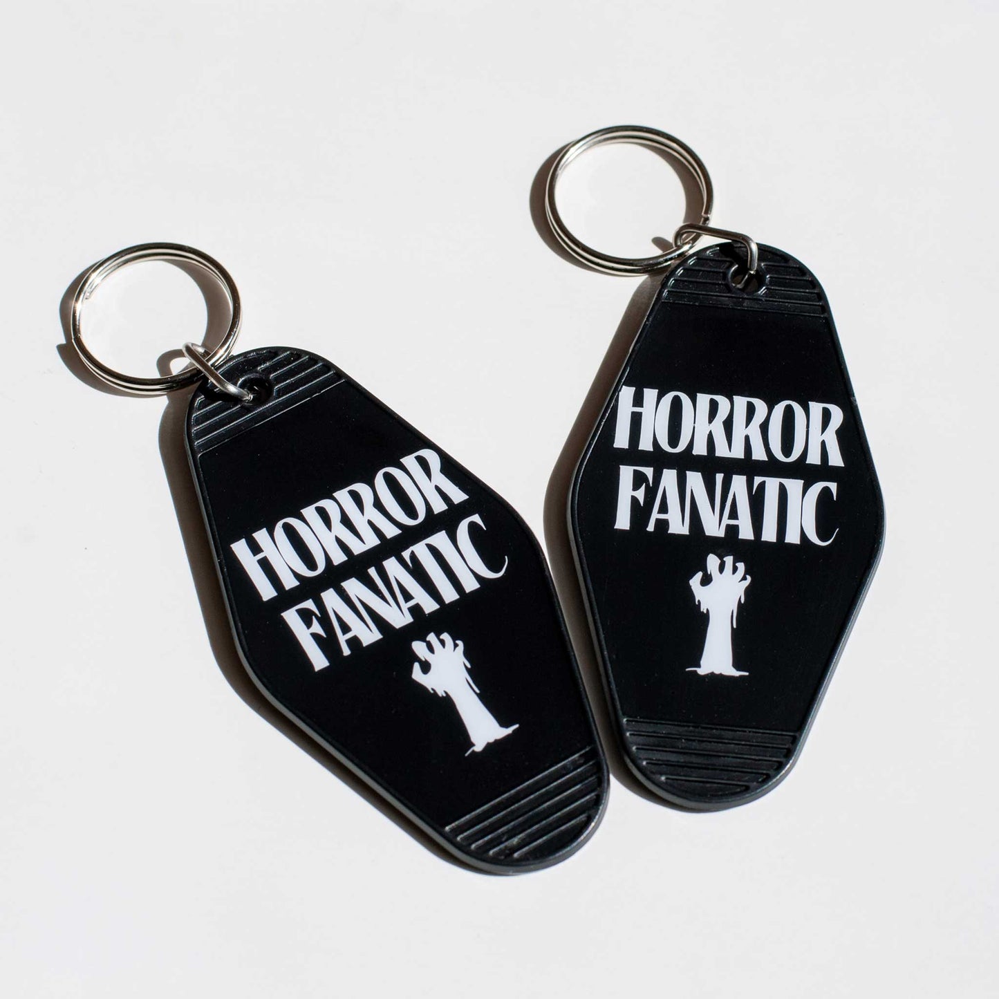 Two black motel keychains with 'Horror Fanatic' text and zombie hand illustrations on a white background