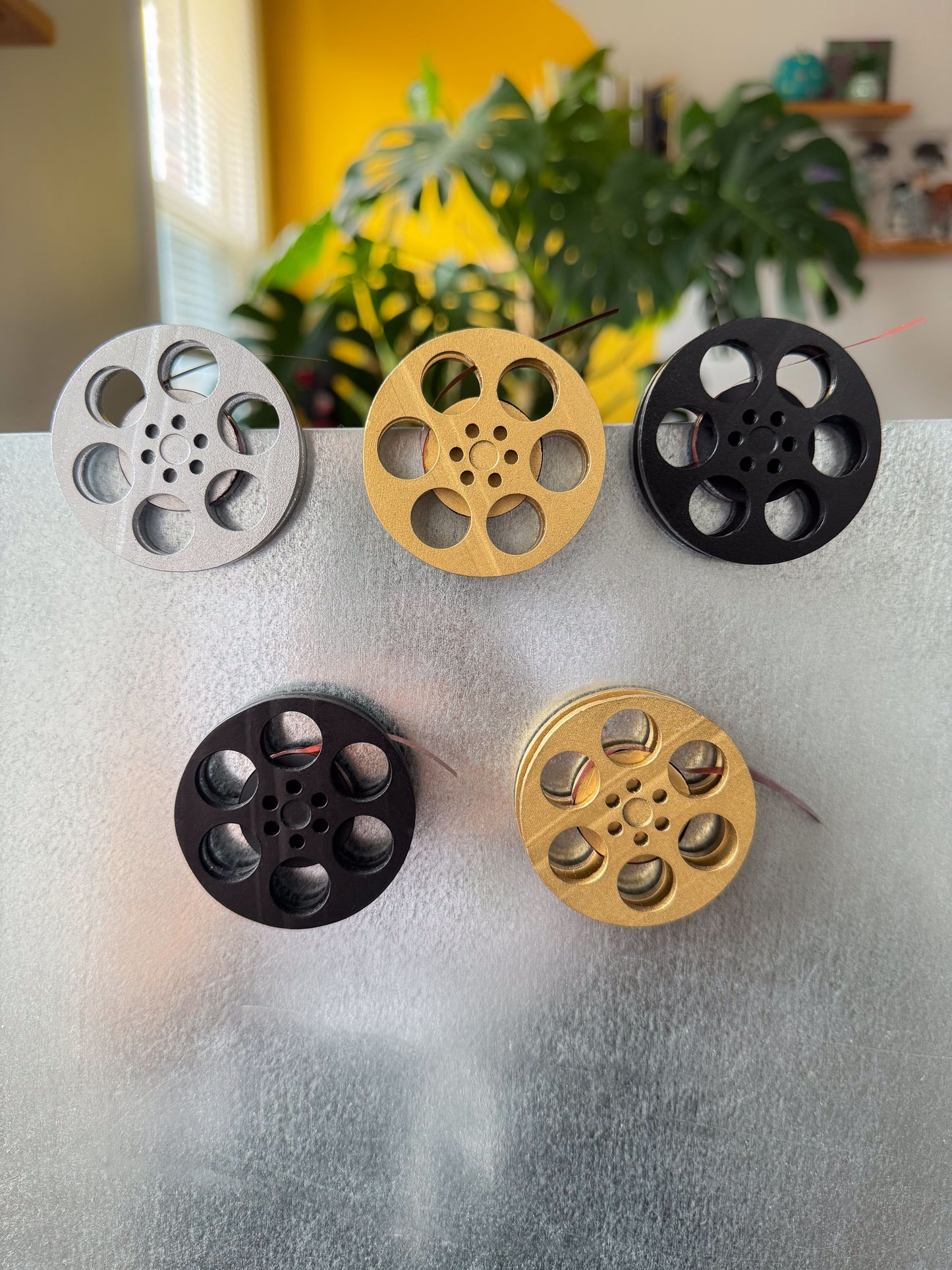 front view of miniature movie reel magnets in gold silver and black holding up a movie ticket on fridge