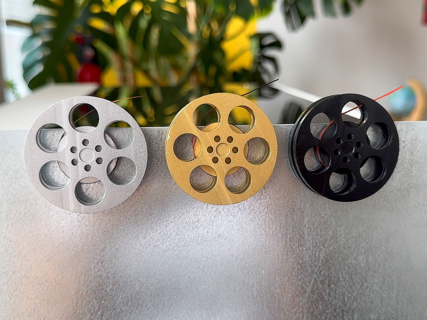front view of three miniature movie reel magnets in gold silver and black holding up a refrigerator
