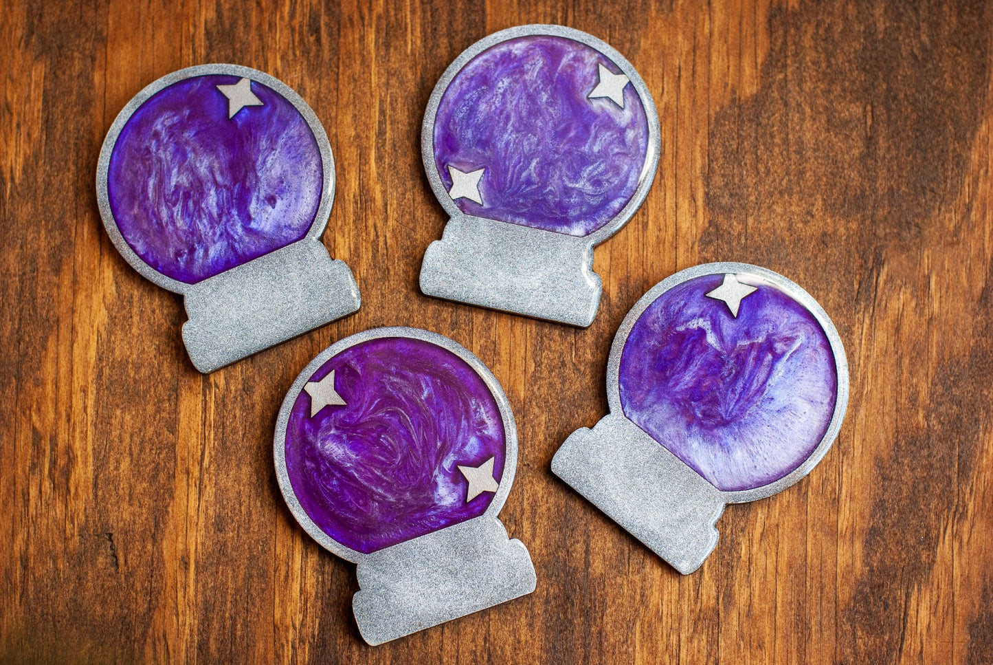 Top down view of purple and silver mystical celestial-themed resin crystal ball coasters on a wooden table and cup of tea