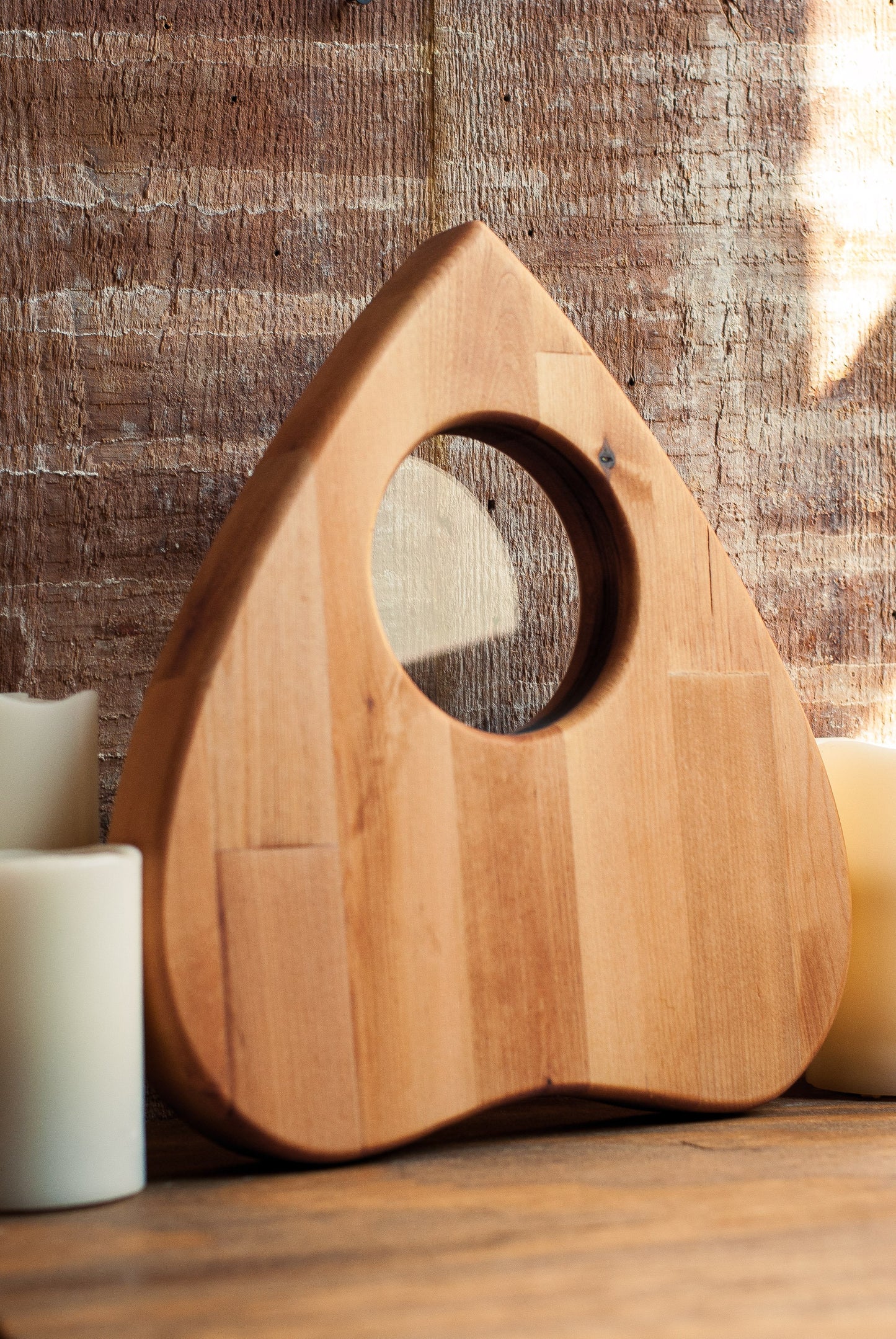 Wooden planchette charcuterie board with a circular looking glass on a wooden surface with candles.