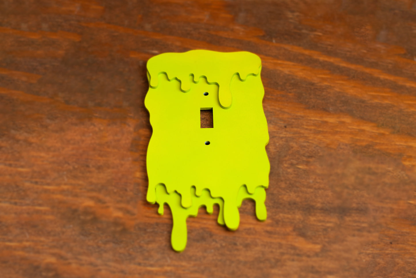 Top down view of a green slime drip light switch cover plate on a wooden table