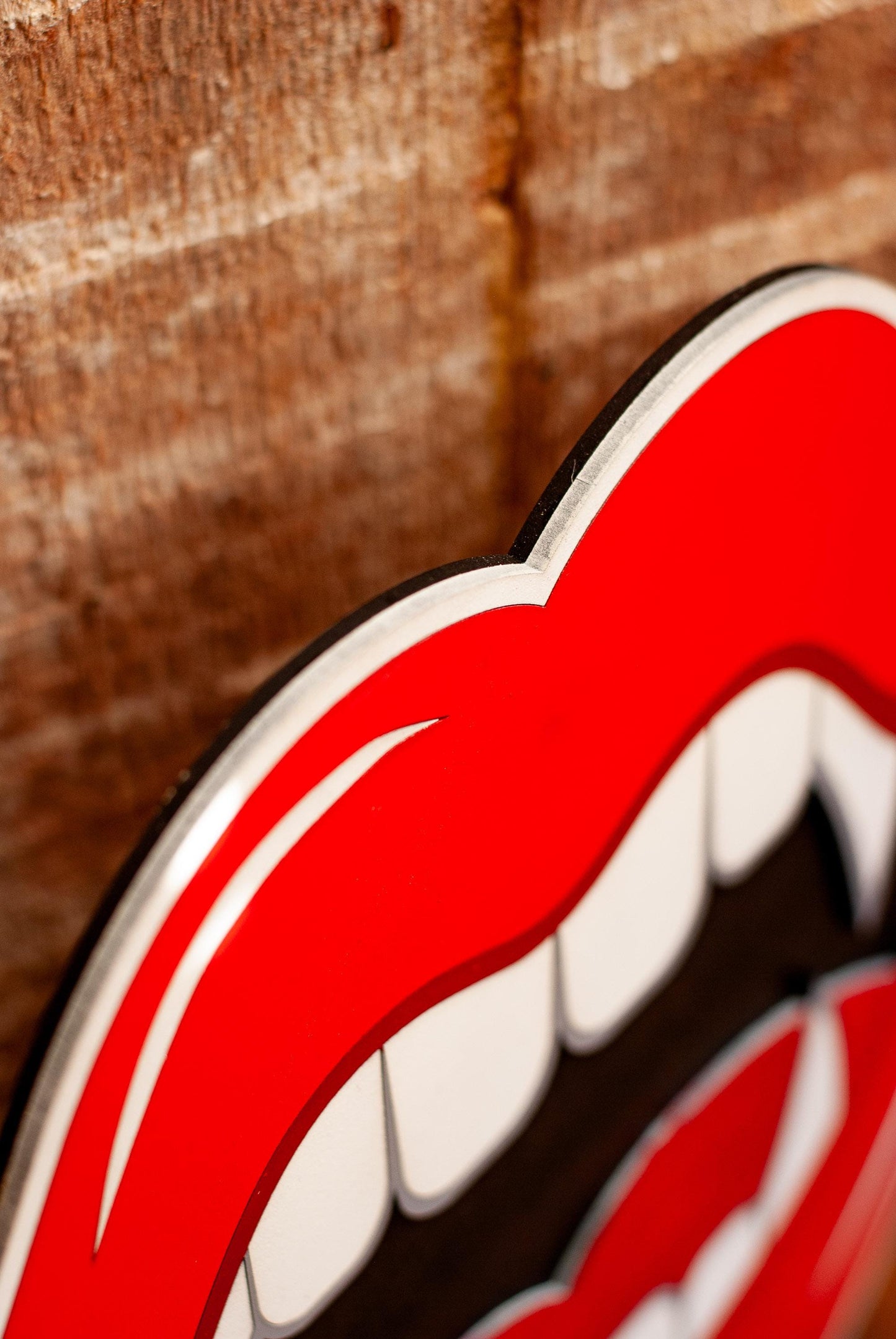 Close-up of a red and white vampire mouth wall art against a wooden background