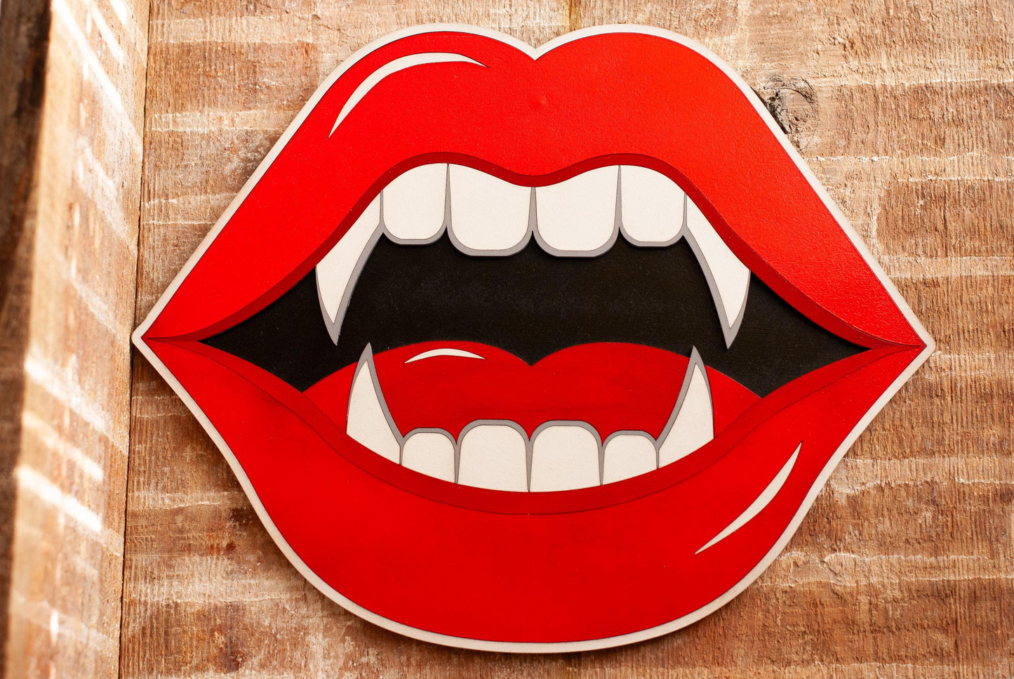 Blood red lips with vampire fangs wall art hanging on a wooden background
