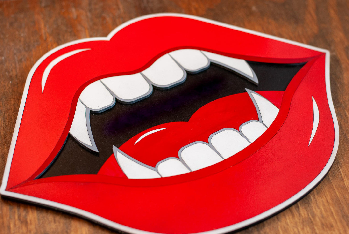 Bright red lips with white vampire fangs laying on a wooden surface