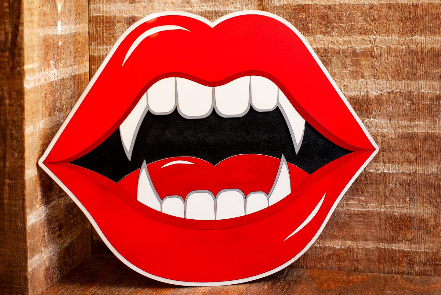 Wooden wall art of red lips with fangs on a wooden background