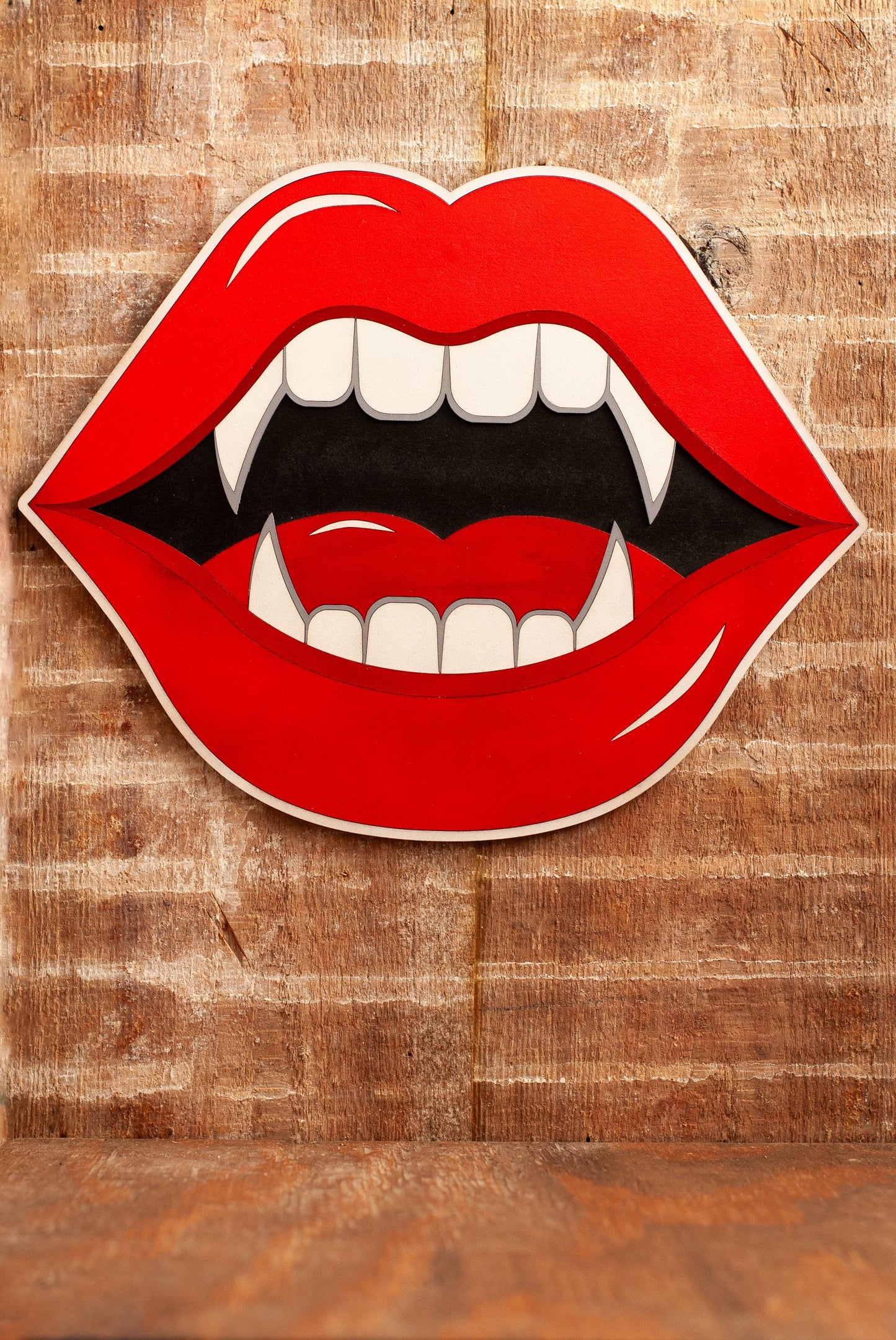 Hanging wooden wall art of Illustrated red lips with fangs on a wooden background