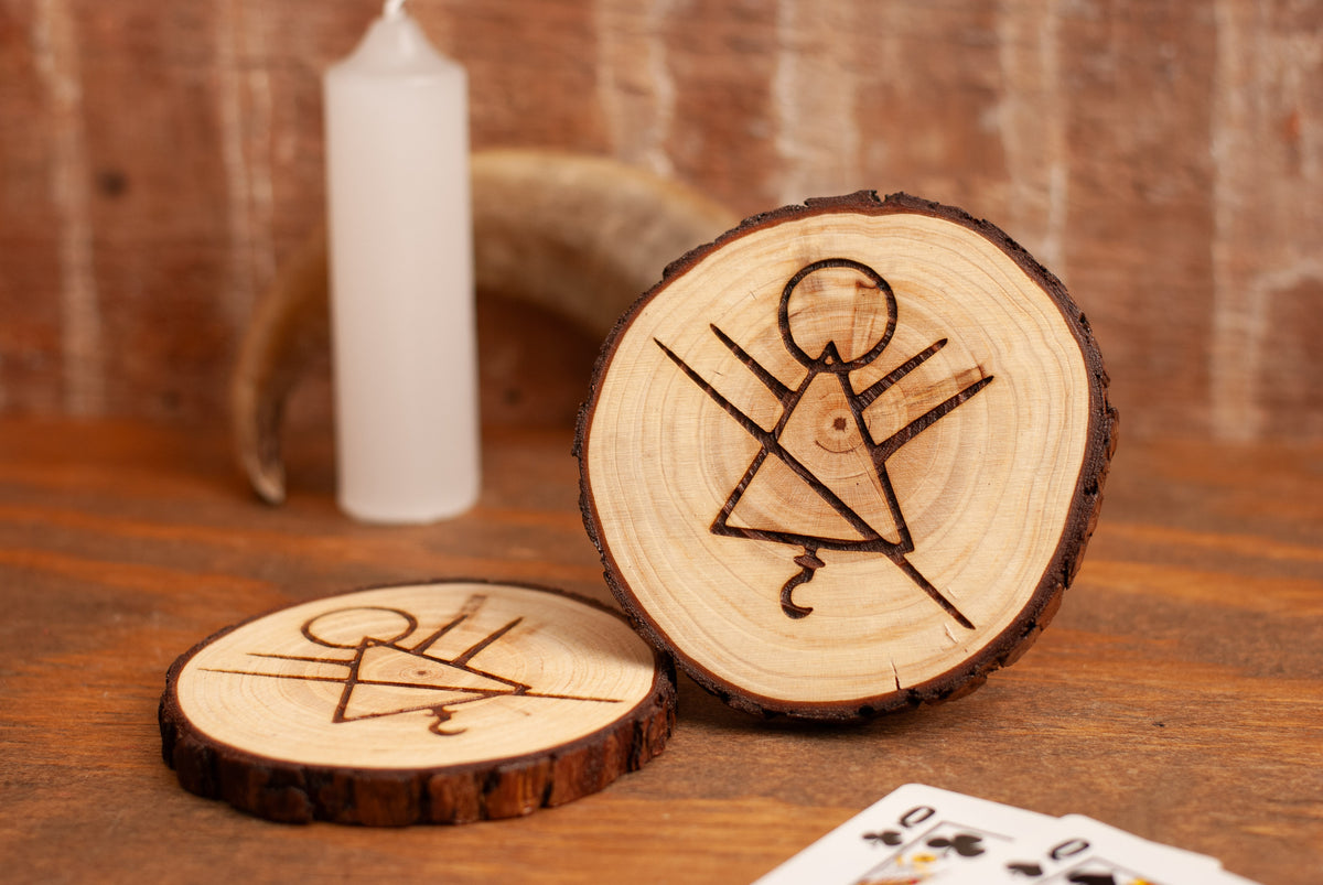 Two wooden coasters with engraved rune symbols on a wooden surface with playing cards in background