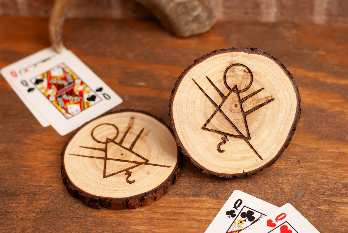 Wooden coasters with engraved stick figure rune symbol designs on a wooden surface with playing cards.