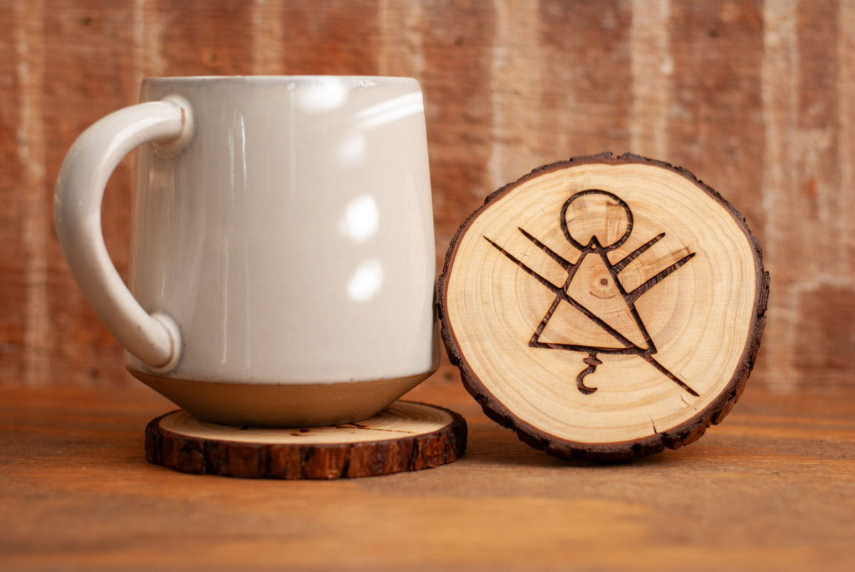 White mug on a wooden coaster with a wooden slice featuring a rune symbol.