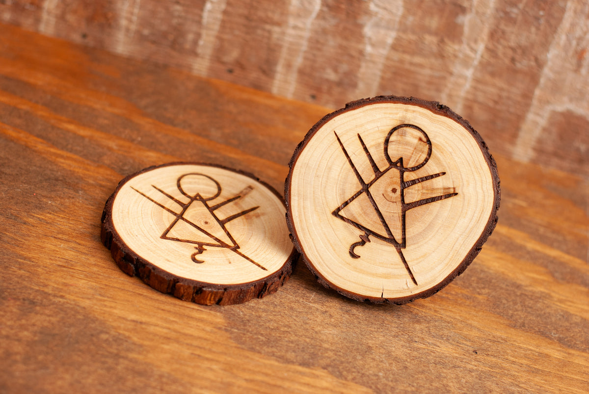 Two wooden coasters with engraved stick figure rune symbol designs on a wooden surface.