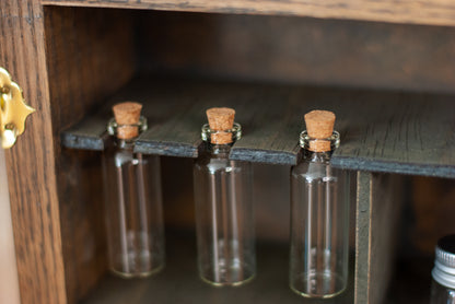 Close-up of three small glass bottles with cork stoppers hanging in a rustic wooden shelf in an apothecary box