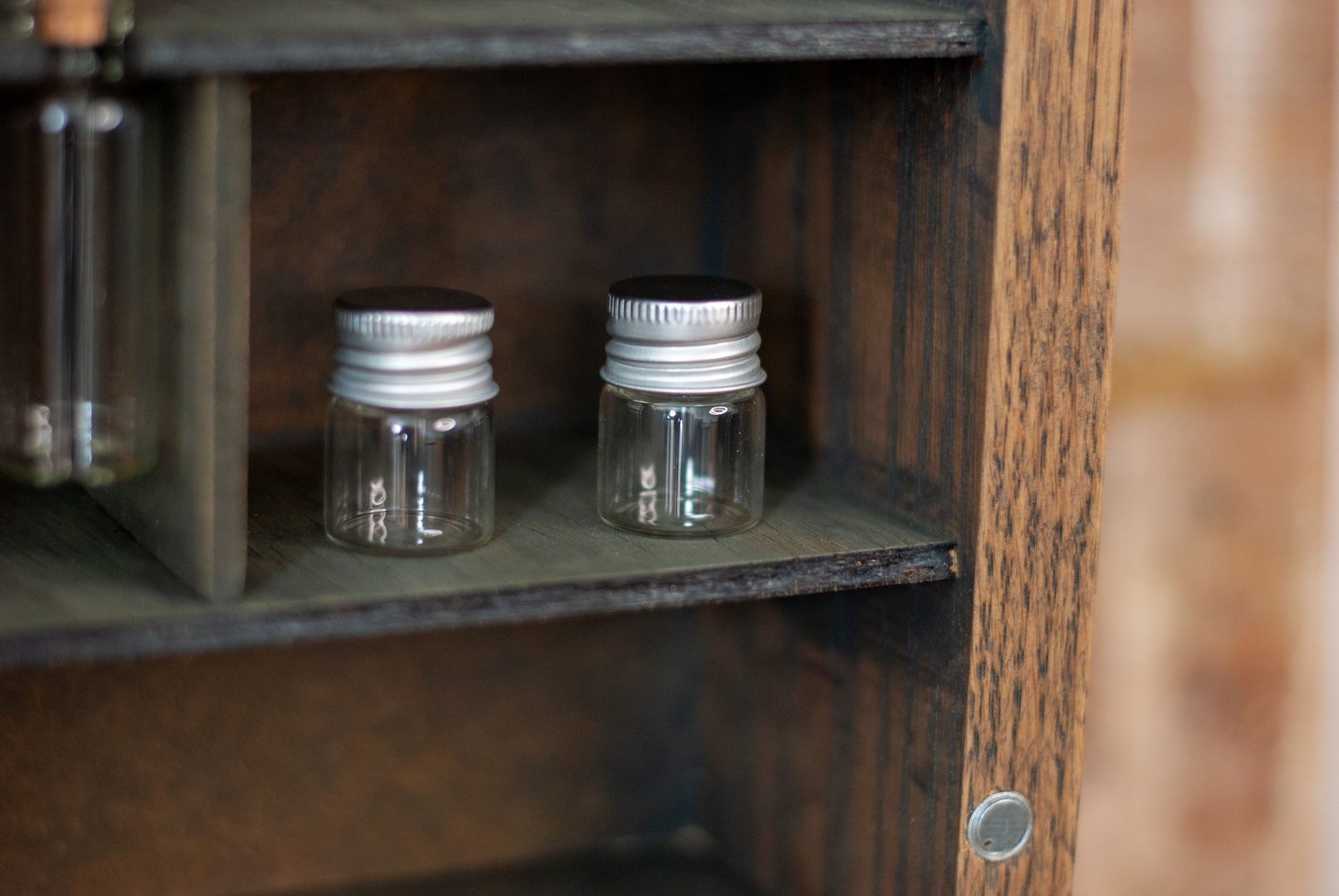 close-up of two small glass jars with metal lids on a rustic wooden shelf in an apothecary box