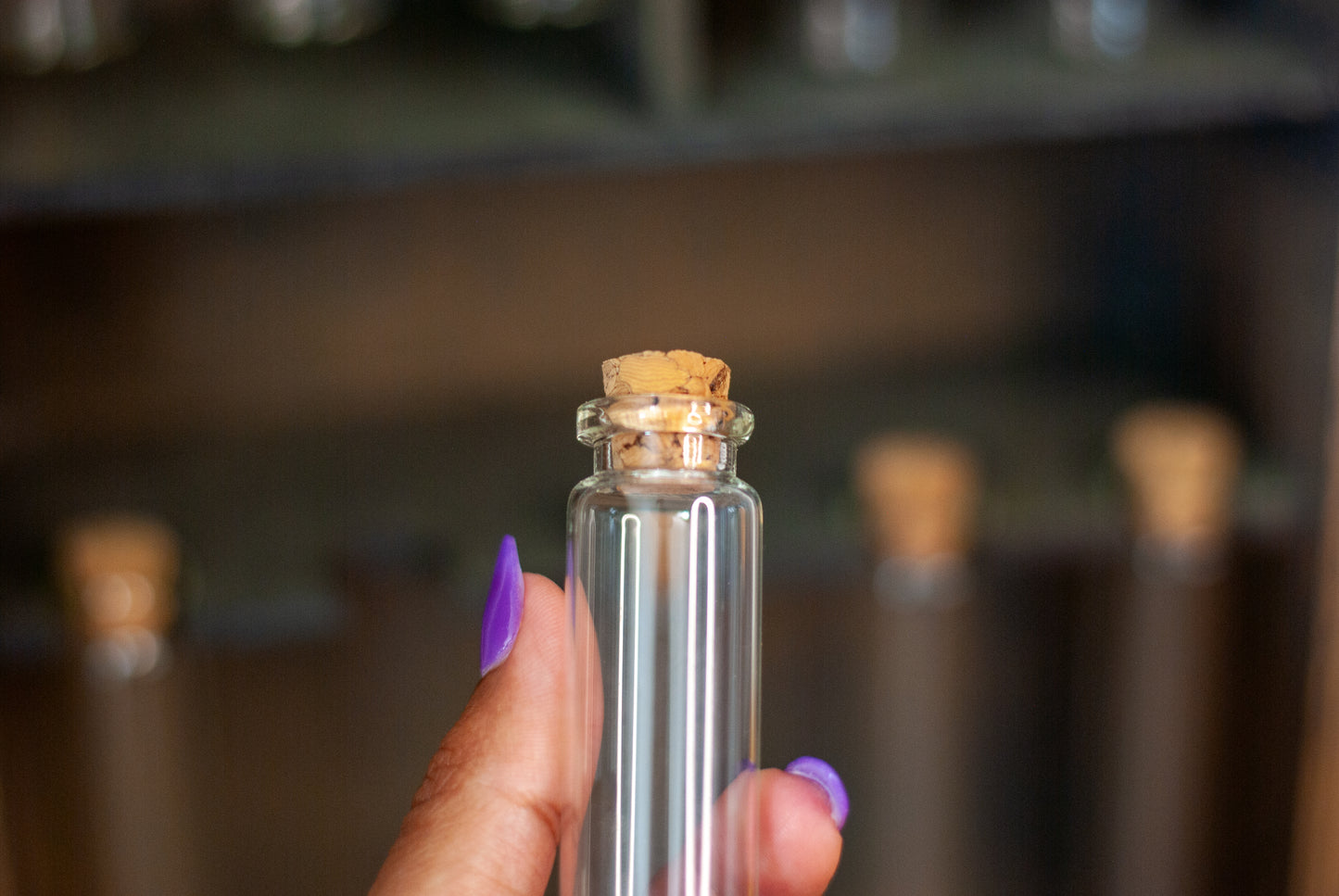 Clear glass vial bottle with cork held by a hand against a blurred background of an apothecary box
