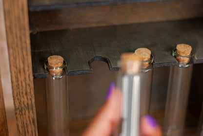 Close-up of a hand holding a small glass vial bottle with a cork against a wooden shelf in a rustic apothecary box