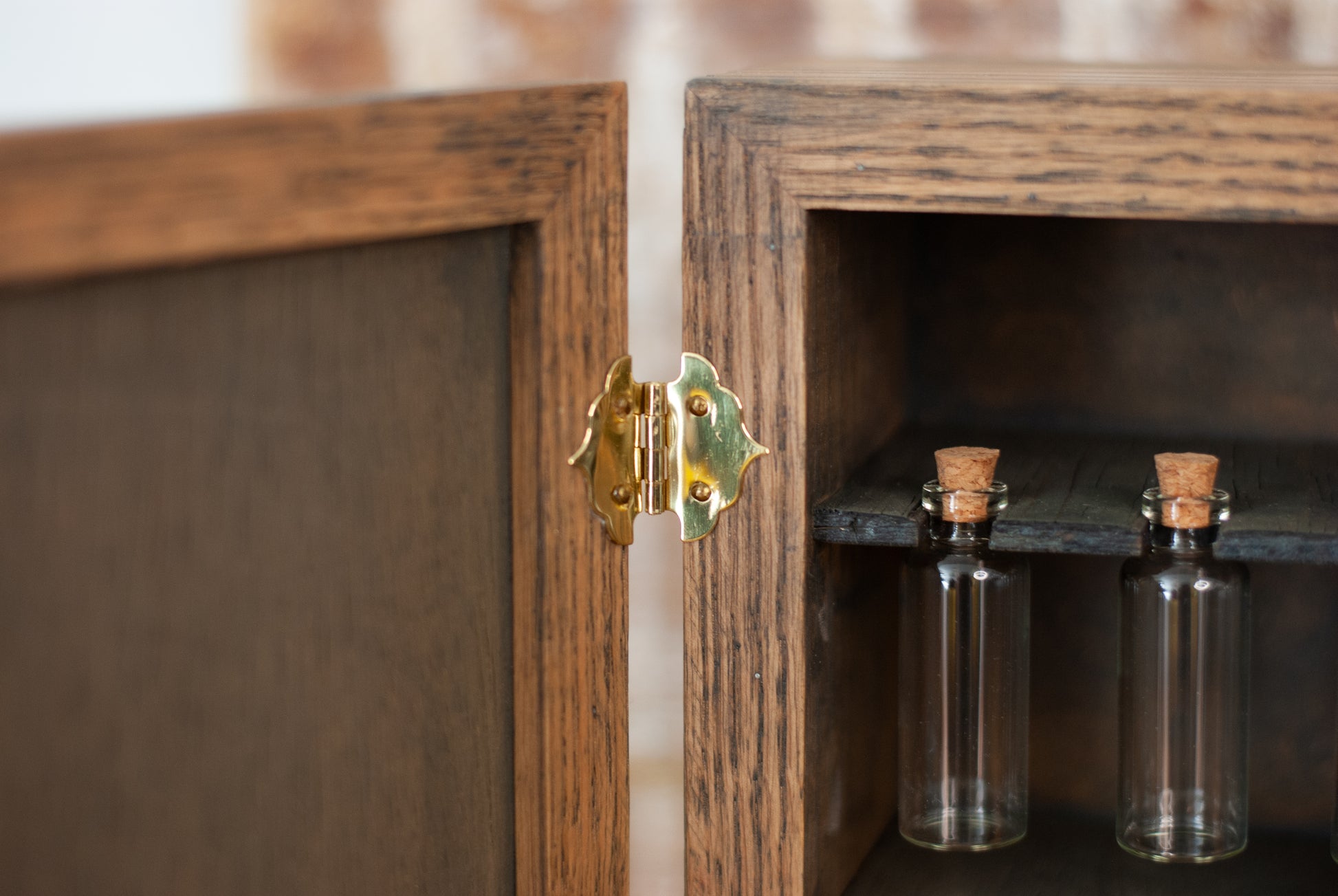 Rustic wooden apothecary cabinet with glass vial bottles inside, featuring a gold hinge.