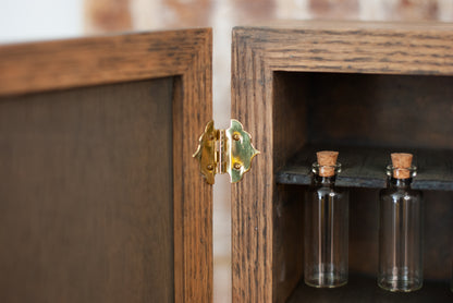 Rustic wooden apothecary cabinet with glass vial bottles inside, featuring a gold hinge.