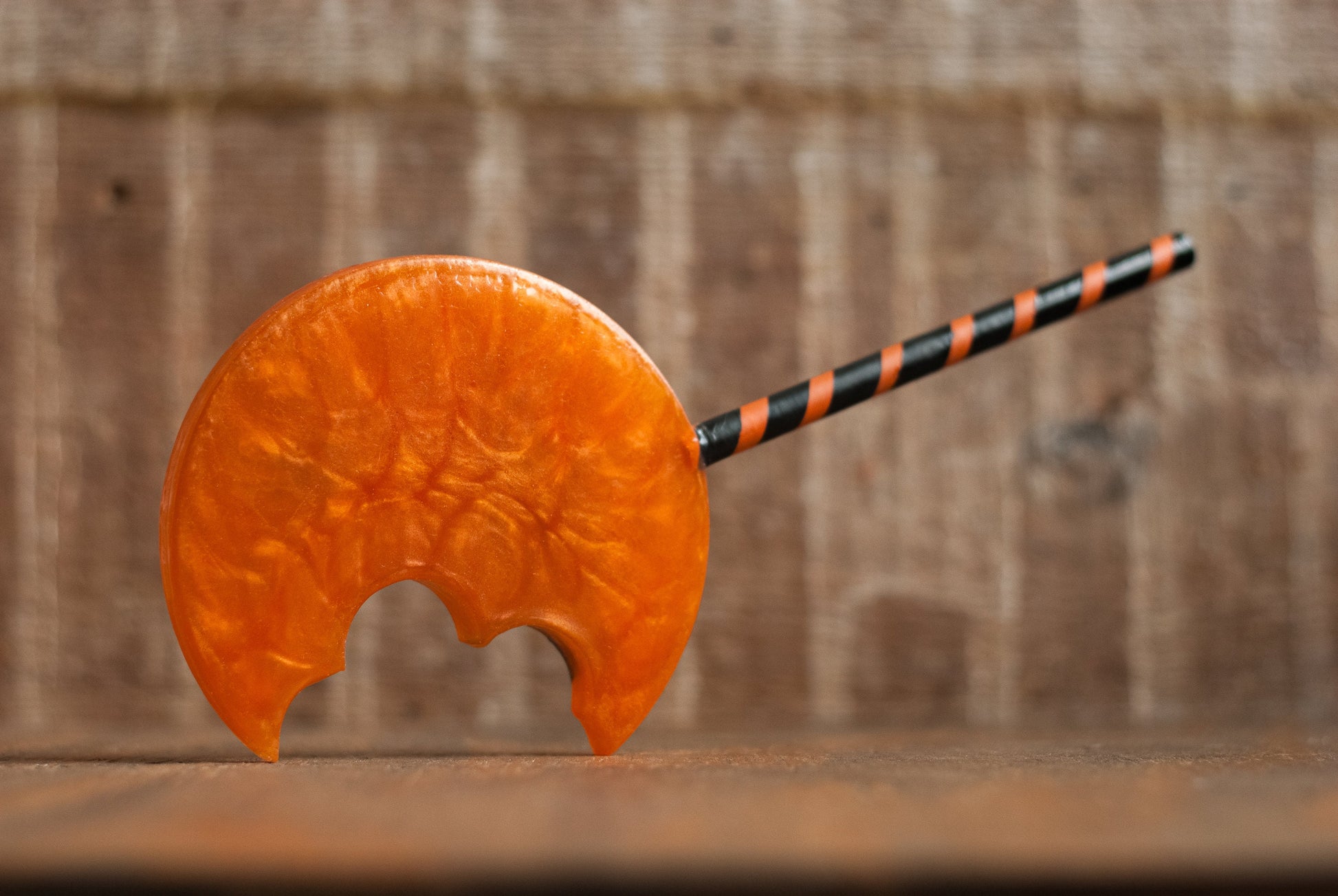 Back of a black and orange Halloween-themed horror movie pumpkin lollipop prop made of resin for trick or treat and cosplay displayed on wooden table