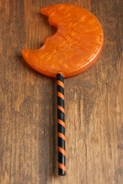 Back view of black and orange Halloween-themed horror movie pumpkin lollipop prop made of resin for trick or treat and cosplay displayed on wooden table