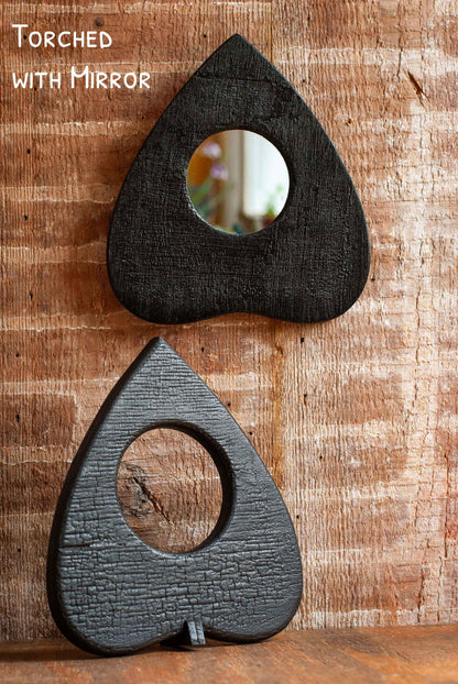 Two teardrop-shaped Ouija Planchette mirrors with a 'Torched' effect on a wooden surface.