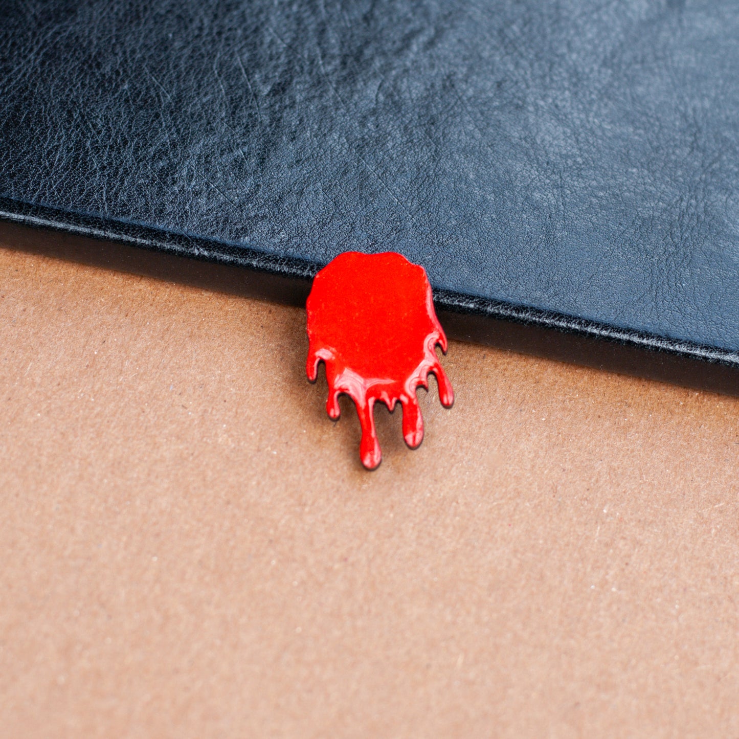 Red wooden pinback style button shaped like a dripping bloodstain on a textured surface