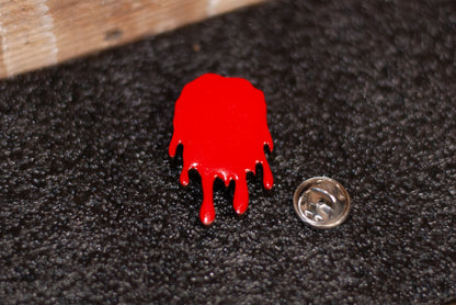 Red blood-like designed pinback style button on a black background with a metal clasp.