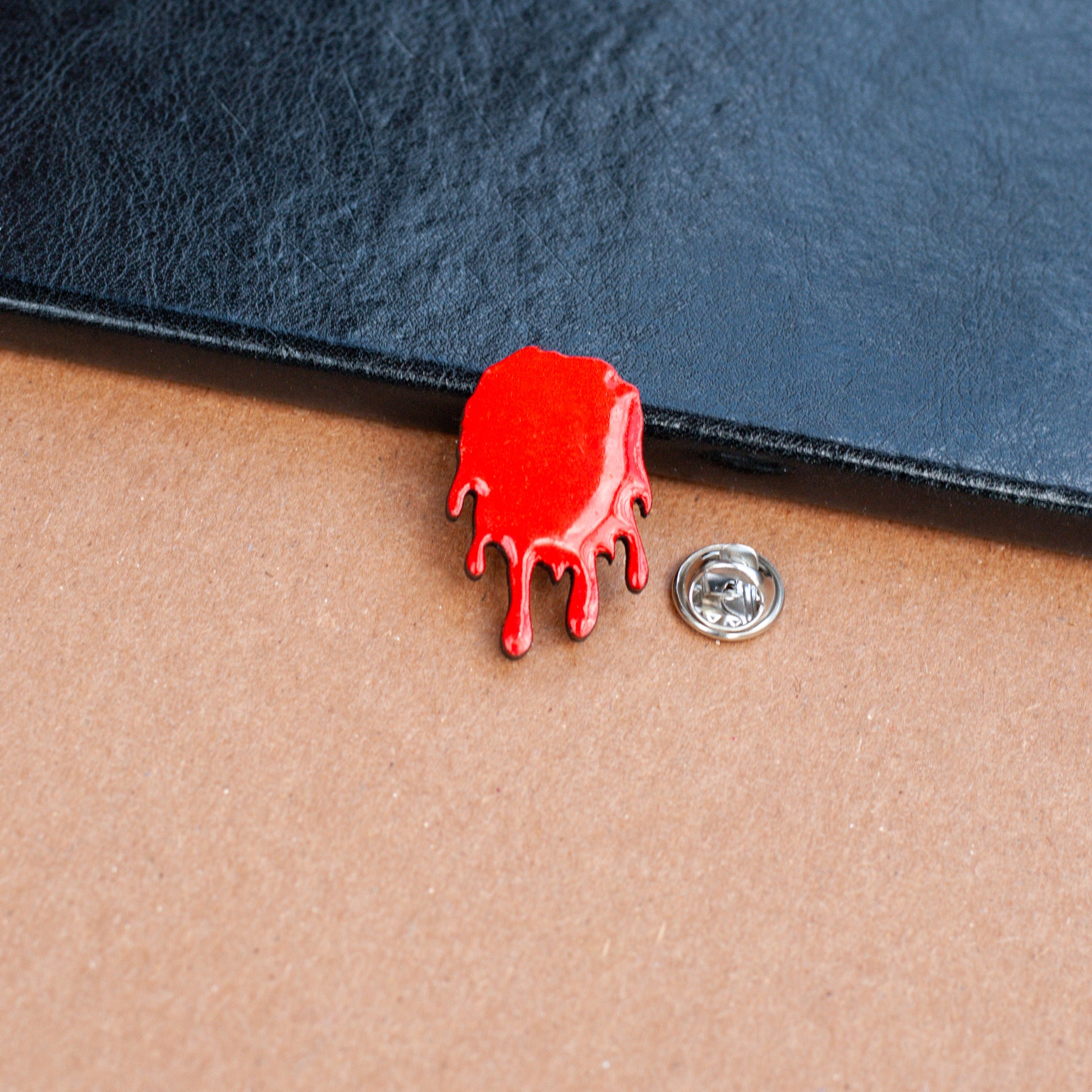 Red wooden pinback style button shaped like a dripping bloodstain on a textured surface with metal clasp