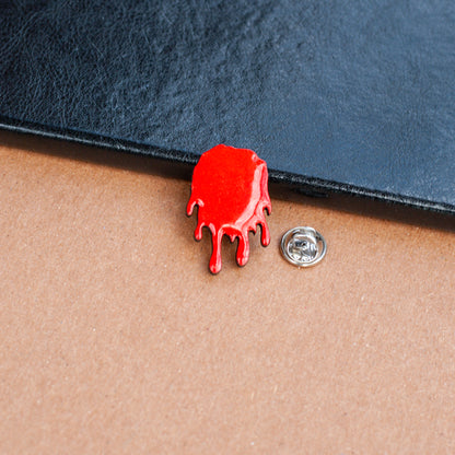 Red wooden pinback style button shaped like a dripping bloodstain on a textured surface with metal clasp