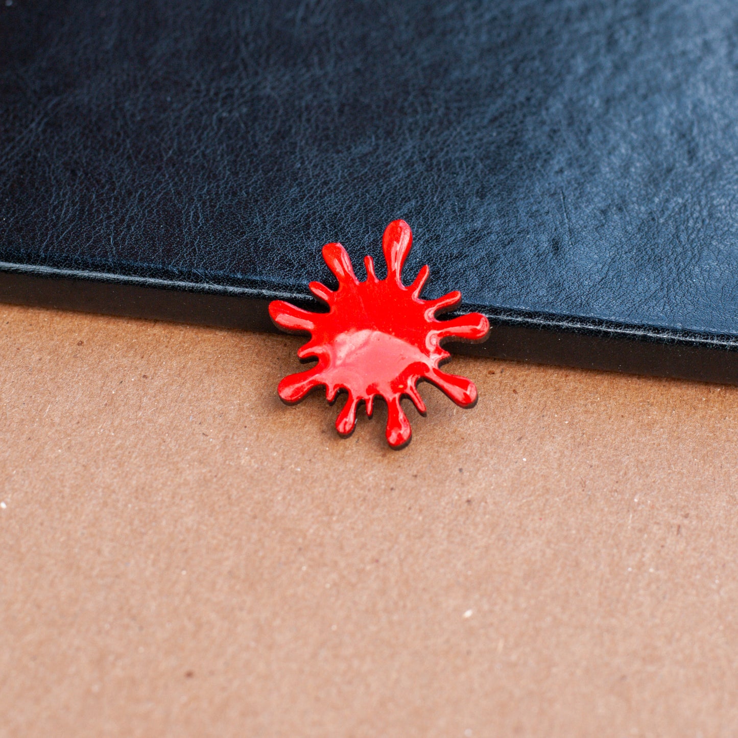 Blood red splatter brooch pin on wooden table with black book in background