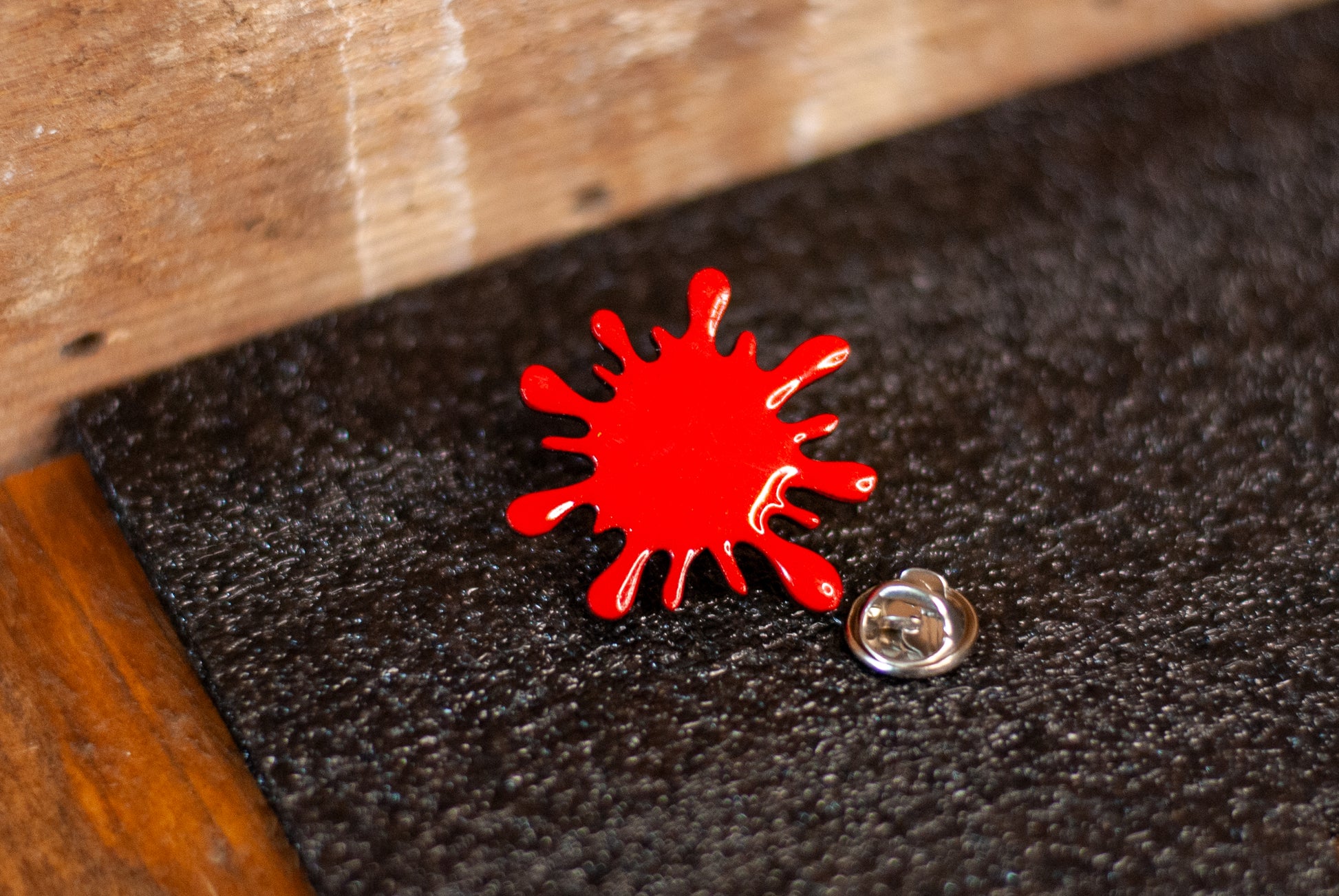 Blood red splatter brooch pin on black and wooden background