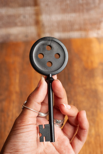 Hand holding a black skeleton button key against a wooden background