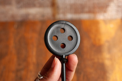 Close-up view of a black Coraline inspired button key movie prop replica on wooden table