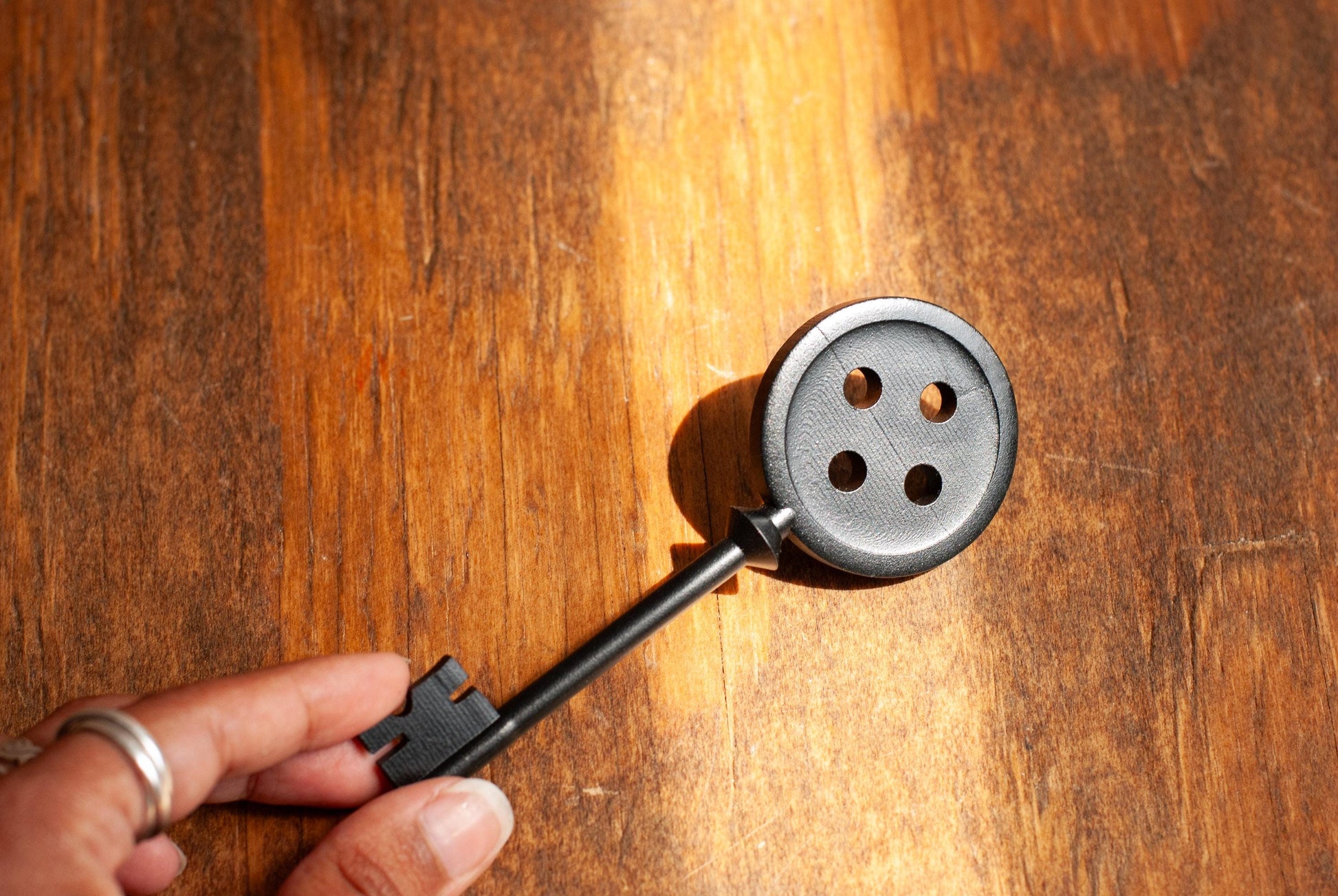 Hand holding a black Coraline inspired button key prop replica on wooden table