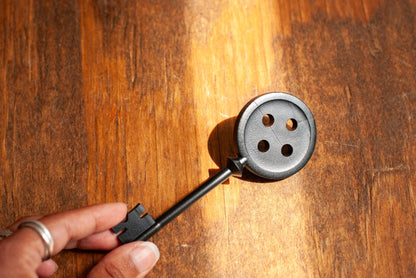 Hand holding a black Coraline inspired button key prop replica on wooden table