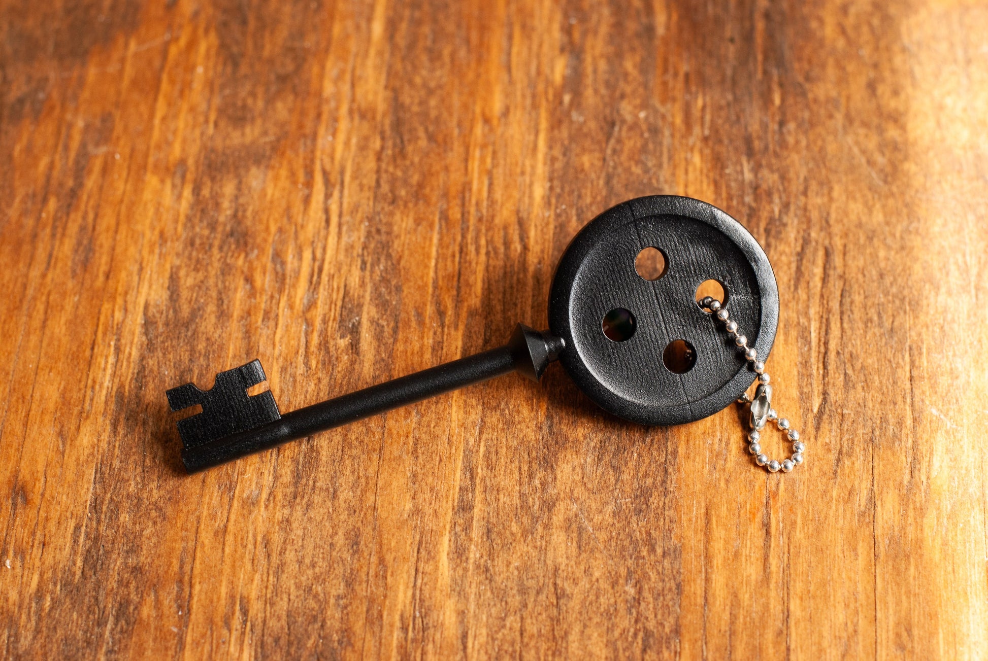 Black Coraline inspired button key prop replica with silver ball chain on wooden table