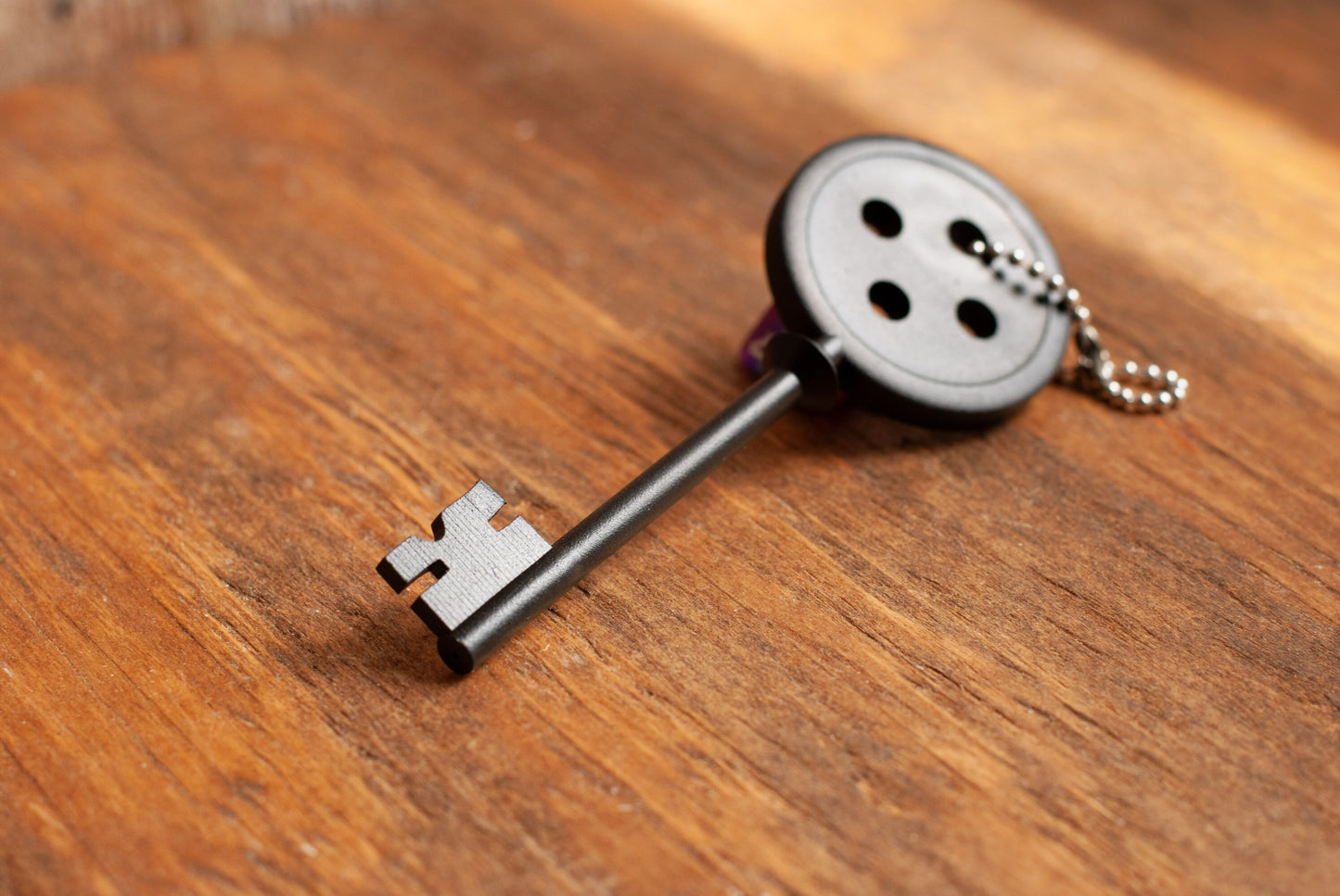 Black Coraline inspired button key prop replica with silver ball chain on wooden table