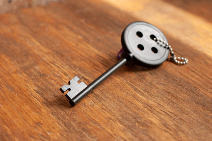 Black Coraline inspired button key prop replica with silver ball chain on wooden table