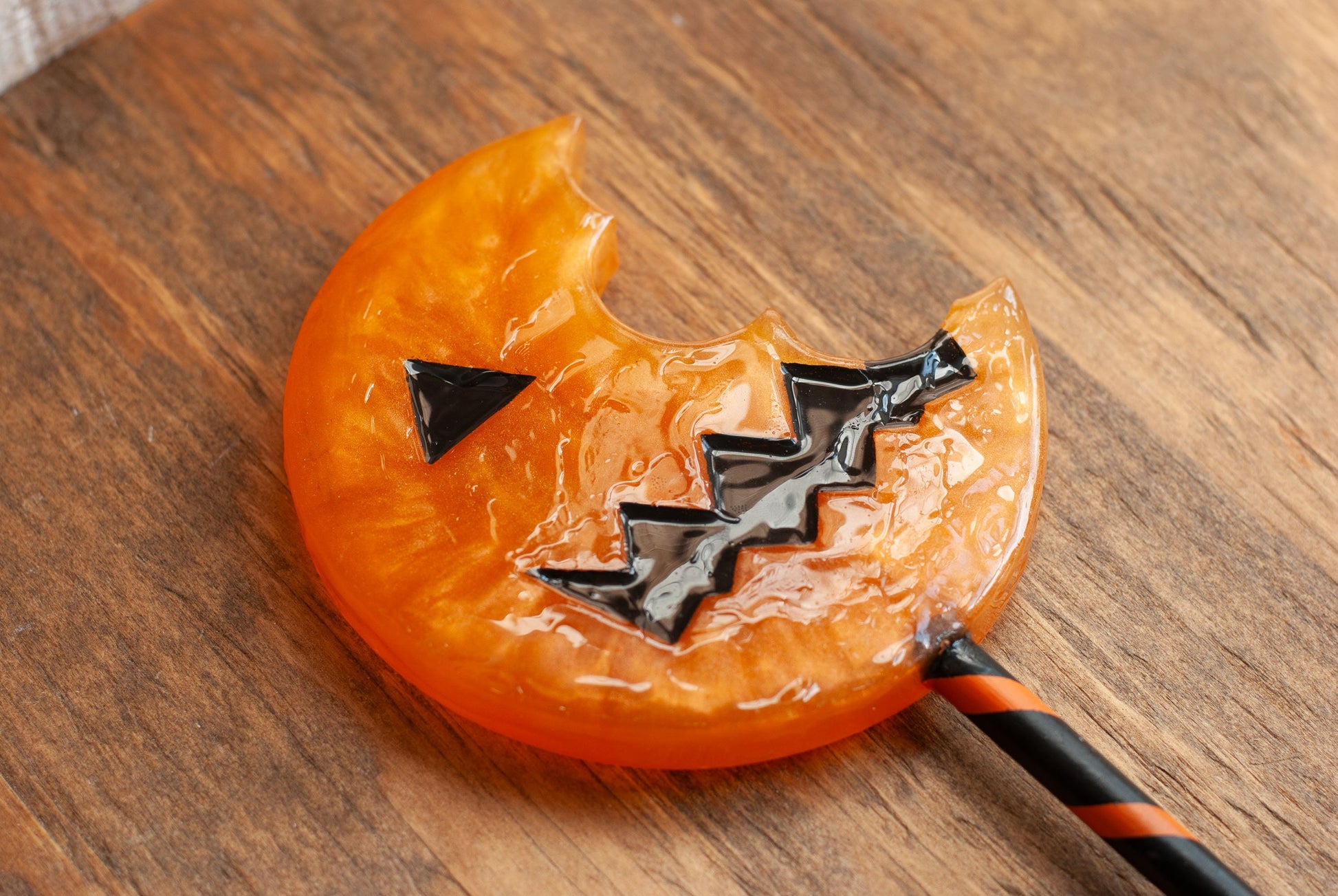 Close up view of a black and orange Halloween-themed horror movie pumpkin lollipop prop made of resin for trick or treat and cosplay displayed on wooden table