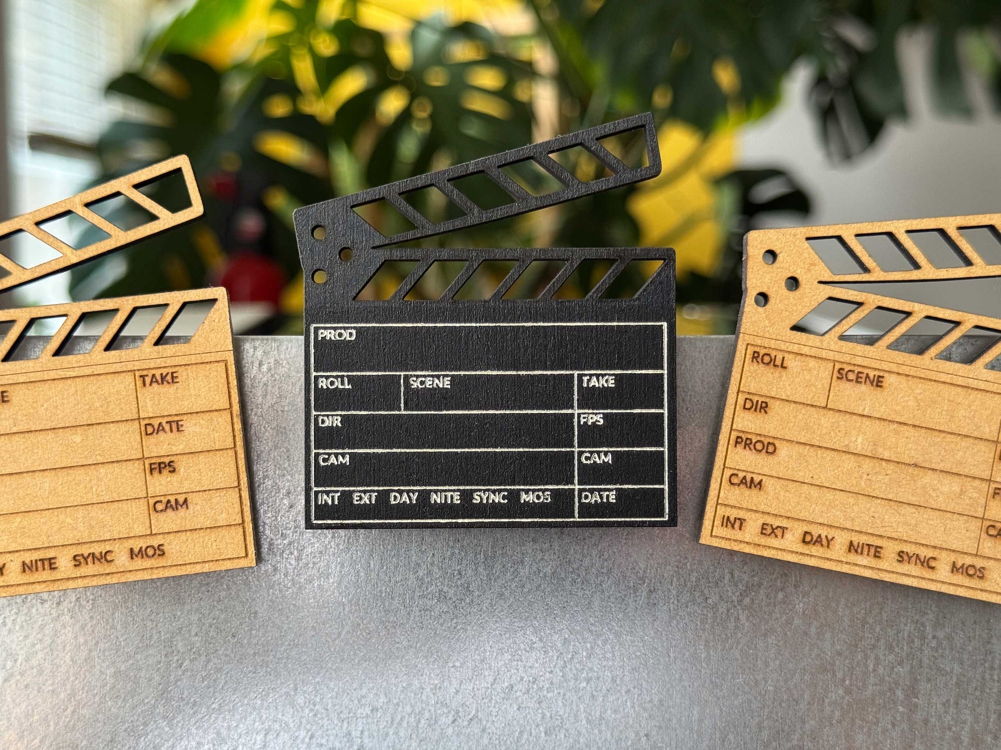 front view of three engraved wooden clapboard magnets in brown and black on a metal fridge in a studio room